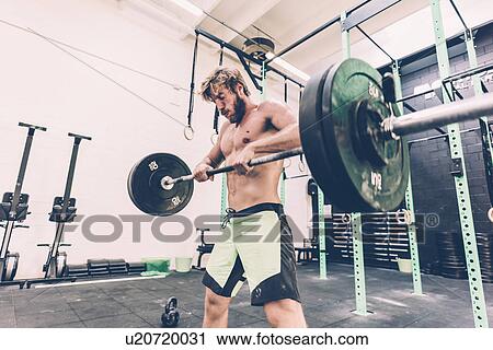 Stock Image - Young man weightlifting barbell in cross training gym. Fotosearch