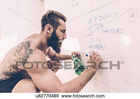 Stock Photo - Young man writing on white board in cross training gym. Fotosearch