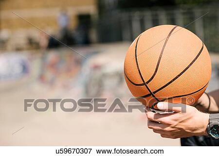 Stock Photo - Young mans hands holding basketball ball in city skatepark. Fotosearch