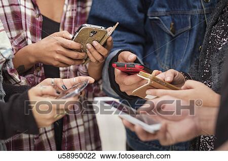 Stock Image - Young people outdoors using smartphones. Fotosearch