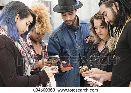 Stock Image - Young people outdoors using smartphones. Fotosearch