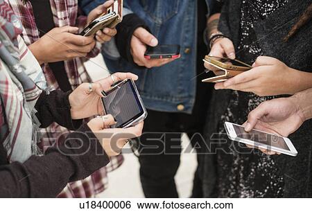 Stock Photograph - Young people outdoors using smartphones. Fotosearch