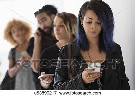 Stock Photo - Young people standing in line using smartphones. Fotosearch