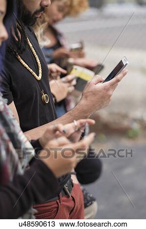 Stock Image - Young people standing in row using smartphones. Fotosearch