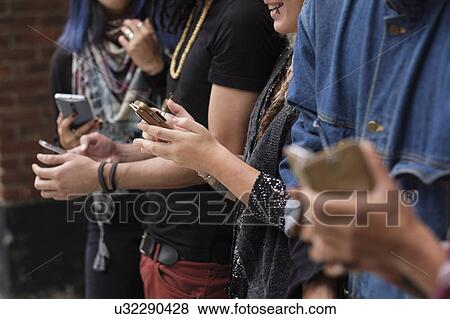 Young people standing in row using smartphones View Large Photo Image Stock Photo - Young people standing in row using smartphones. Fotosearch