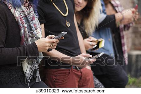 Stock Photo - Young people standing in row using smartphones. Fotosearch