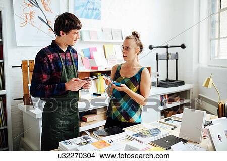 Picture - Young woman chatting to young male craftsman and using tablet technology to make purchase in art bookshop. Fotosearch