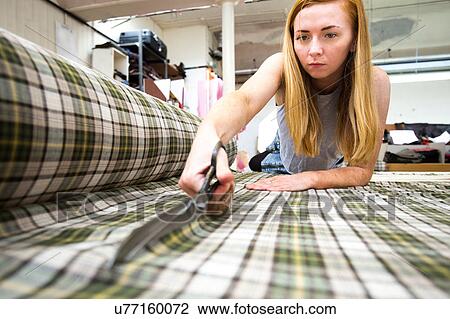 Stock Image - Young woman cutting fabric in leather jacket manufacturers. Fotosearch