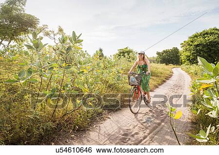 Stock Photograph - Young woman cycling on dirt track, Gili Meno, Lombok, Indonesia. Fotosearch