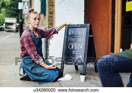 Young woman kneeling on pavement, looking up and resting hand on blackboard View Large Photo Image Stock Image - Young woman kneeling on pavement, looking up and resting hand on blackboard. Fotosearch