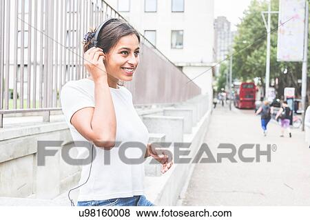 Young woman outdoors, wearing headphones, smiling View Large Photo Image Stock Photo - Young woman outdoors, wearing headphones, smiling. Fotosearch