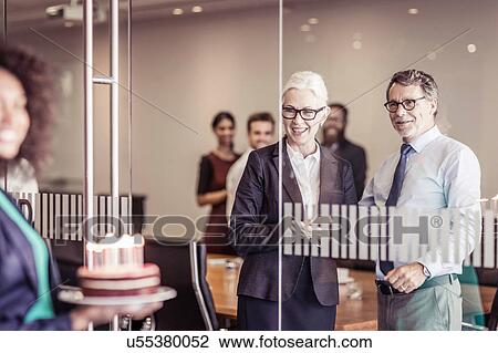 Stock Image - Young woman presenting cake to business team in boardroom. Fotosearch