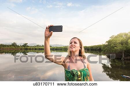Young woman taking smartphone selfie in front of lake, Gili Meno, Lombok, Indonesia View Large Photo Image Stock Image - Young woman taking smartphone selfie in front of lake, Gili Meno, Lombok, Indonesia. Fotosearch
