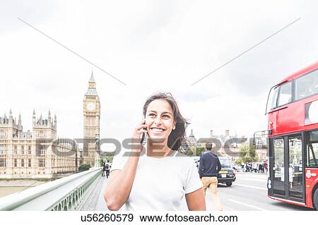 Stock Photo - Young woman using smartphone, houses of parliament and Big Ben in background, London, England. Fotosearch