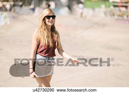 Stock Image - Young woman walking with skateboard in skatepark. Fotosearch