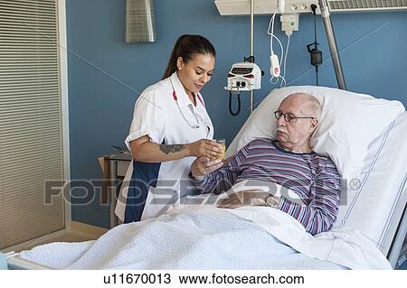 Stock Image - Female nurse giving male patient fruit juice. Fotosearch