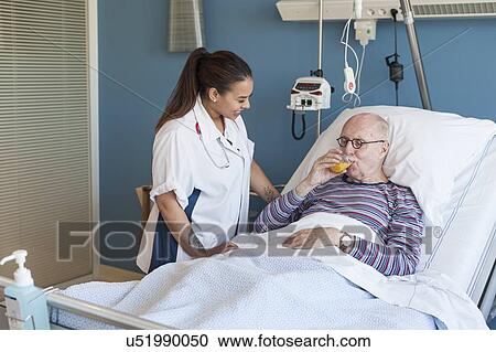 Stock Image - Female nurse with male patient drinking juice. Fotosearch