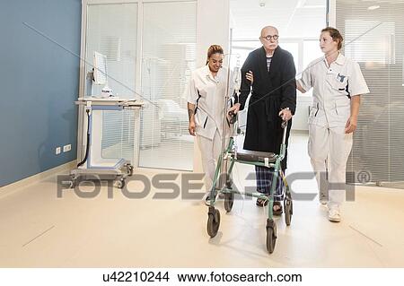 Nurses helping senior male to walk corridor View Large Photo Image Picture - Nurses helping senior male to walk corridor. Fotosearch