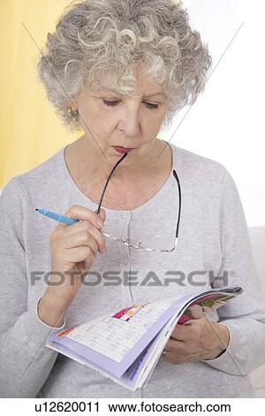 Stock Image - Woman reading magazine holding glasses. Fotosearch