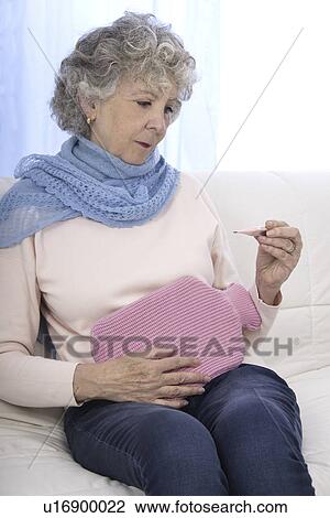 Stock Image - Woman with hot water bottle and thermometer. Fotosearch