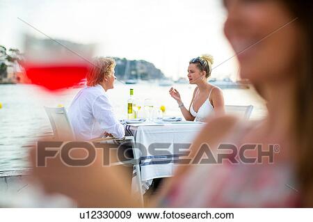 Stock Photo - Background view of young couple at waterfront restaurant, Majorca, Spain. Fotosearch