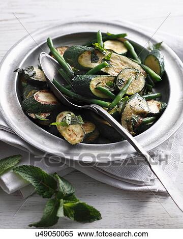 Stock Photography - Bistro table with bowl of buttered courgettes, mint and green beans. Fotosearch