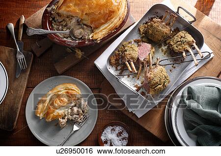 Stock Photograph - Bistro table with herb crusted lamb racks and rustic chicken pie. Fotosearch