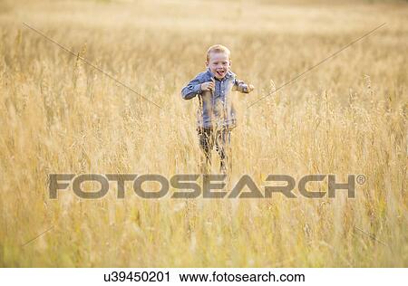 Stock Image - Boy (4-5) running in dry grass. Fotosearch