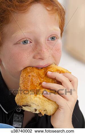 Stock Image - Boy eating pain au chocolate. Fotosearch