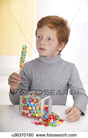 Stock Image - Boy holding lollipop with jar of sweets. Fotosearch