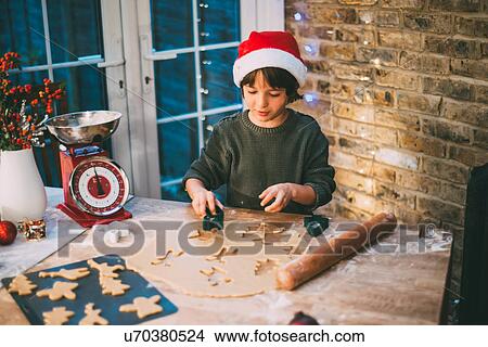 Picture - Boy in Santa hat preparing Christmas cookies at kitchen counter. Fotosearch