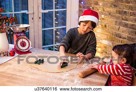 Stock Photograph - Boy preparing Christmas cookies with baby brother at kitchen counter. Fotosearch