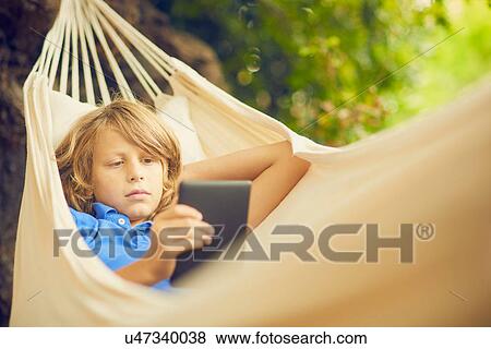 Stock Photo - Boy reclining in garden hammock browsing digital tablet. Fotosearch