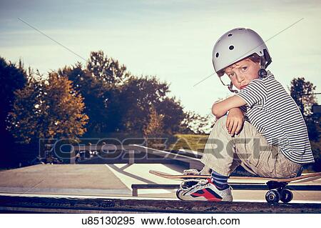 Stock Photography - Boy sitting on skateboard in park. Fotosearch