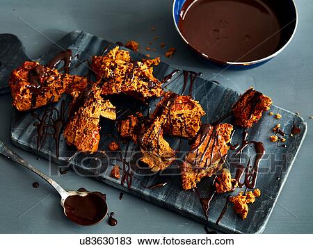 Stock Image - Broken honeycomb toffee with melted chocolate garnish on marble cutting board. Fotosearch