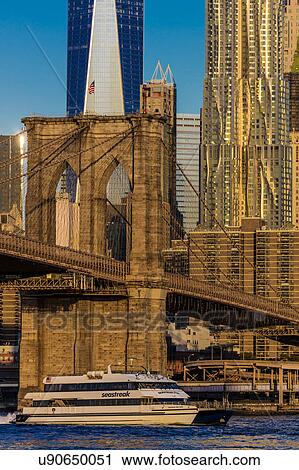 Stock Image - Brooklyn Bridge and Manhattan Skyline features One World Trade Center at Sunrise, NY NY. Fotosearch