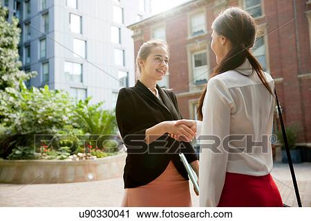Stock Image - Businesswomen shaking hands at meeting, London. Fotosearch