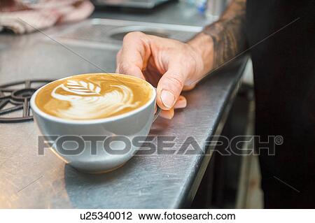 Stock Image - Close up of barista's hand and cup of coffee. Fotosearch