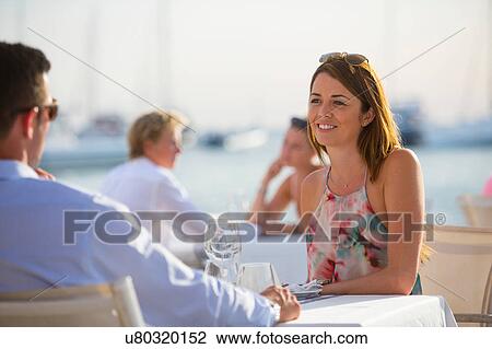 Stock Image - Couple chatting at waterfront restaurant, Majorca, Spain. Fotosearch