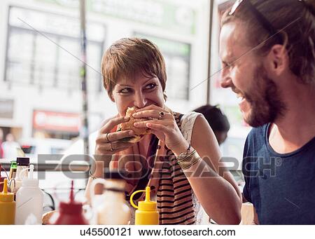 Stock Image - Couple eating burgers at sidewalk cafe, Cape Town, South Africa. Fotosearch