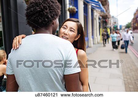 Stock Image - Couple greeting with kiss on cheek at sidewalk cafe. Fotosearch