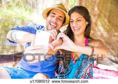 Couple making heart shape with hands taking selfie View Large Photo Image Stock Image - Couple making heart shape with hands taking selfie. Fotosearch