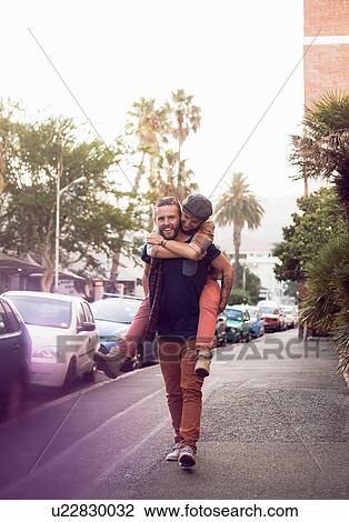 Stock Image - Couple piggybacking on street, Cape Town, South Africa. Fotosearch