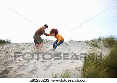 Stock Image - Couple playing at top of sand dune. Fotosearch