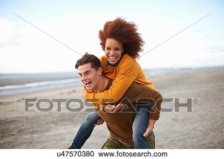 Stock Image - Couple playing piggyback on beach. Fotosearch