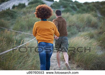 Stock Image - Couple running on grassy dune. Fotosearch