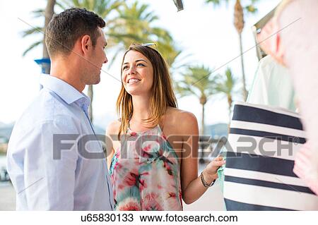 Stock Image - Couple shopping for beach bag at shop front, Majorca, Spain. Fotosearch