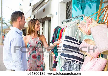 Stock Photo - Couple shopping for beach bag at shop front, Majorca, Spain. Fotosearch