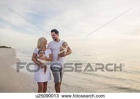 Stock Image - Couple with twins (2-5 months) walking along seashore. Fotosearch