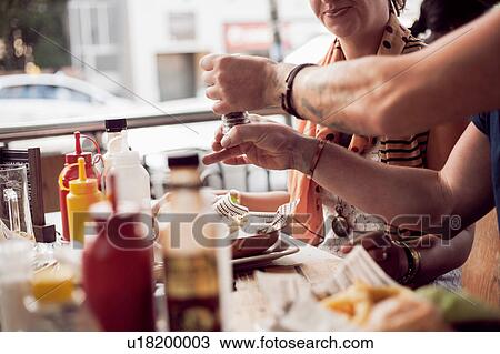 Stock Image - Cropped shot of couple putting pepper on crisps at sidewalk cafe. Fotosearch